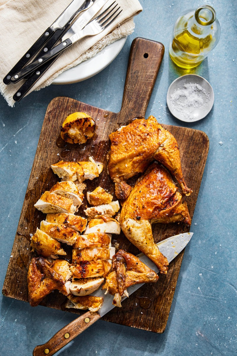 A roasted half chicken, carved on a wooden board with lemon, olive oil and salt