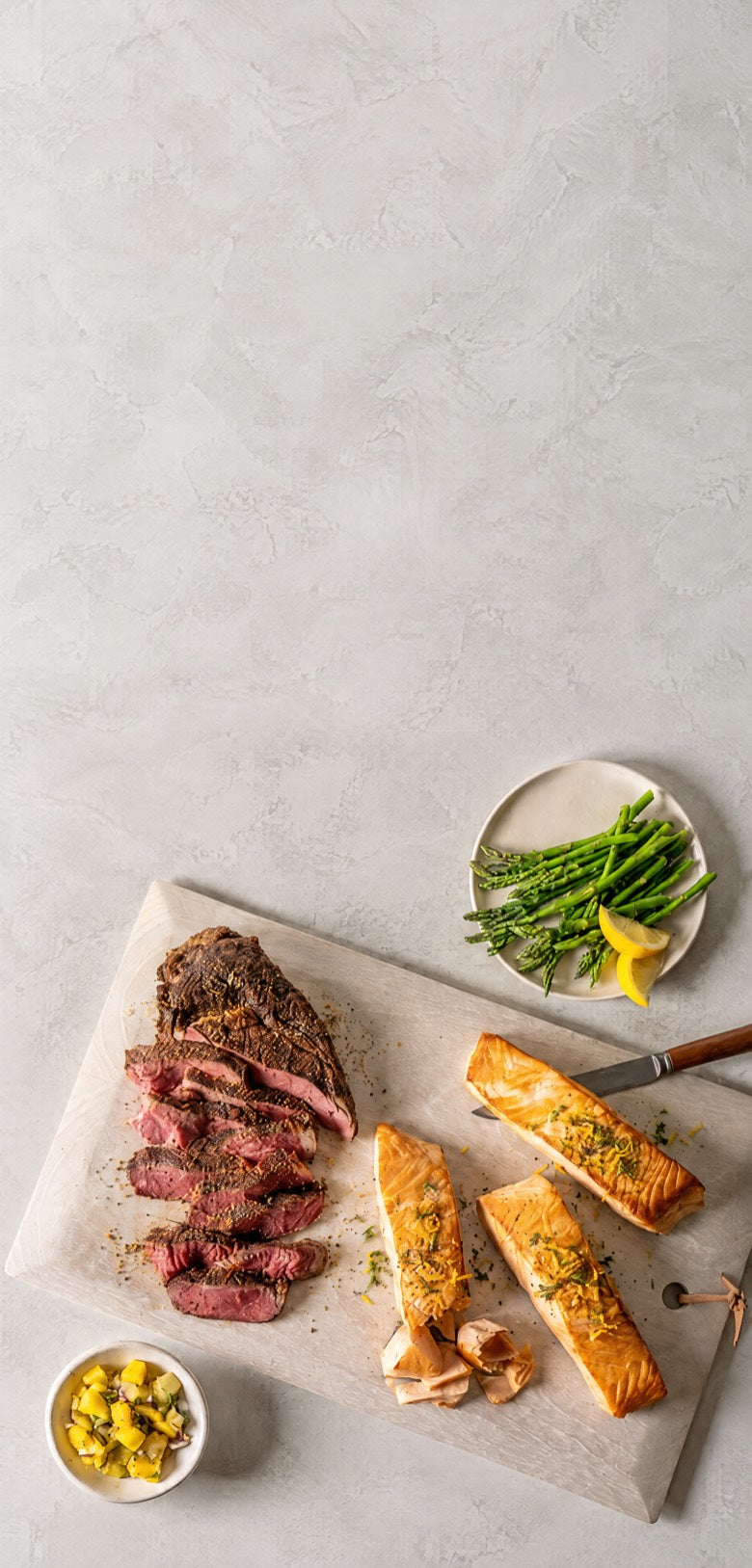 Sliced steak and seared salmon fillets on a serving board with asparagus and lemon