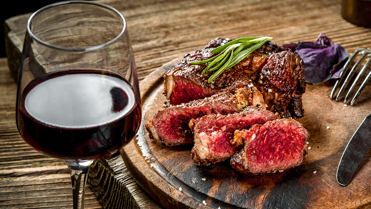 Wine with Steak Grilled ribeye beef steak with red wine, herbs and spices on wooden table